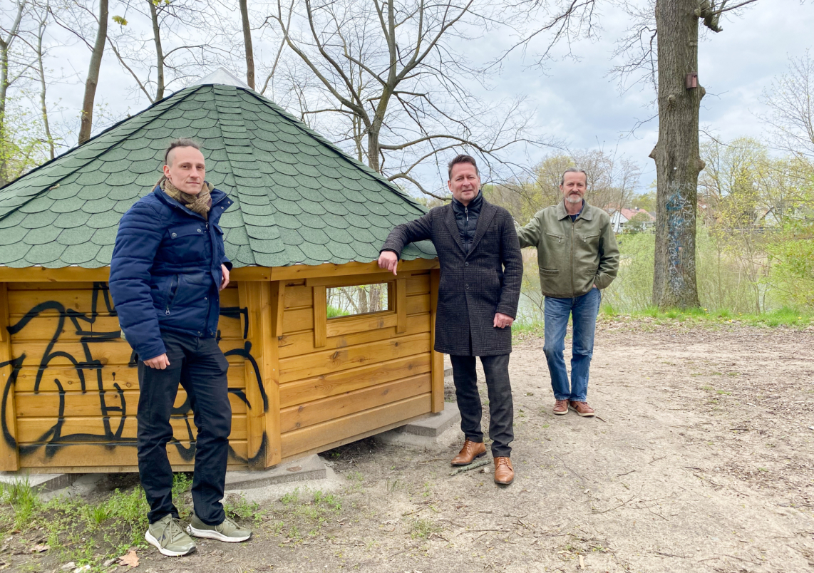 Die Streetworker Steven Blank (links) und Andreas Witt (rechts) präsentieren die neue Wetterschutzhütte am Börnersee mit Bürgermeister Steffen Apelt.