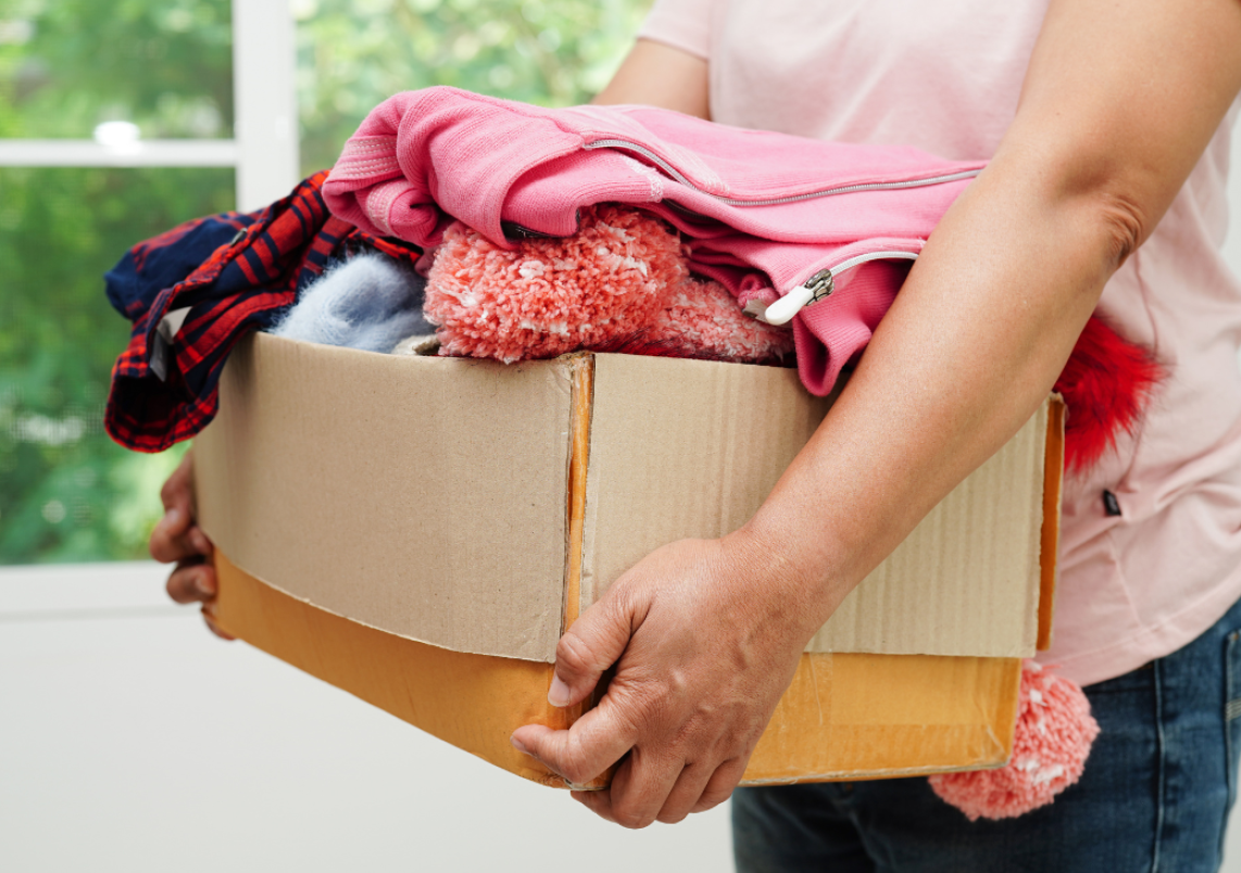 Eine Kiste mit aussortierten Kleidern wird getragen.