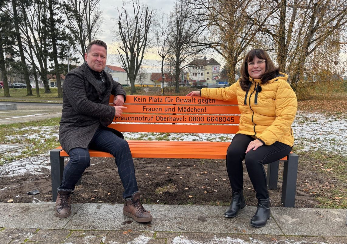 Bürgermeister Steffen Apelt und Gleichstellungsbeauftragte Ramona Lopitz sitzen auf der Anti-Gewalt-Bank am Rathausplatz ein.