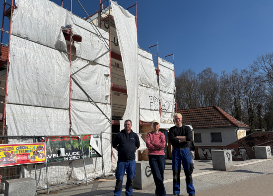 Künstlerin Barbara Trautmann hat mit den Arbeiten an der Fassade des Kulturbahnhofs begonnen. Künstlerin Barbara Trautmann und Mitarbeiter der Werkstatt für Metallgestaltung "Fittkau" stehen vor dem Bahnhof Hohen Neuendorf.